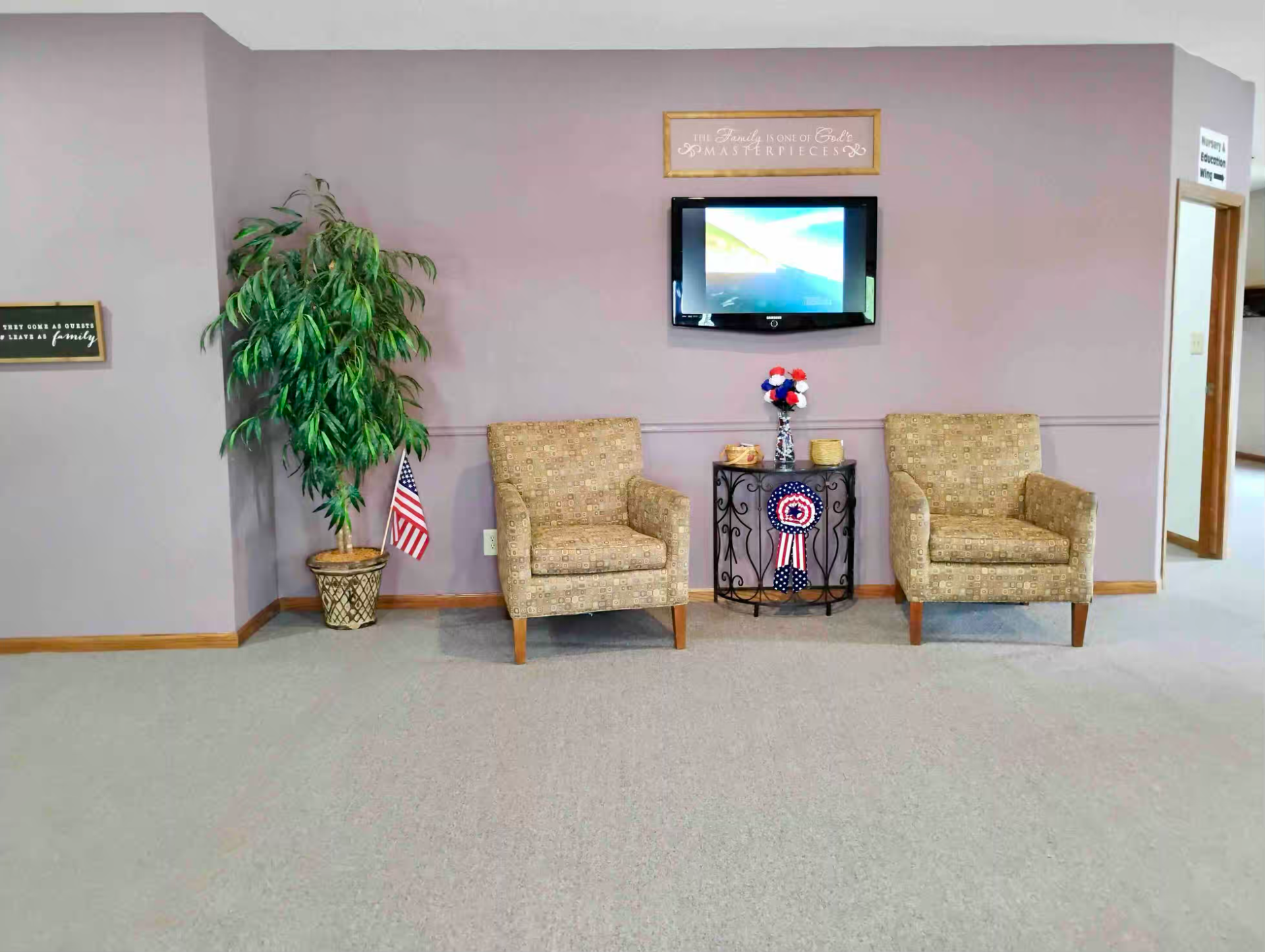 Seating area with two beige armchairs, wall TV, potted plant, and decorations in a lobby.