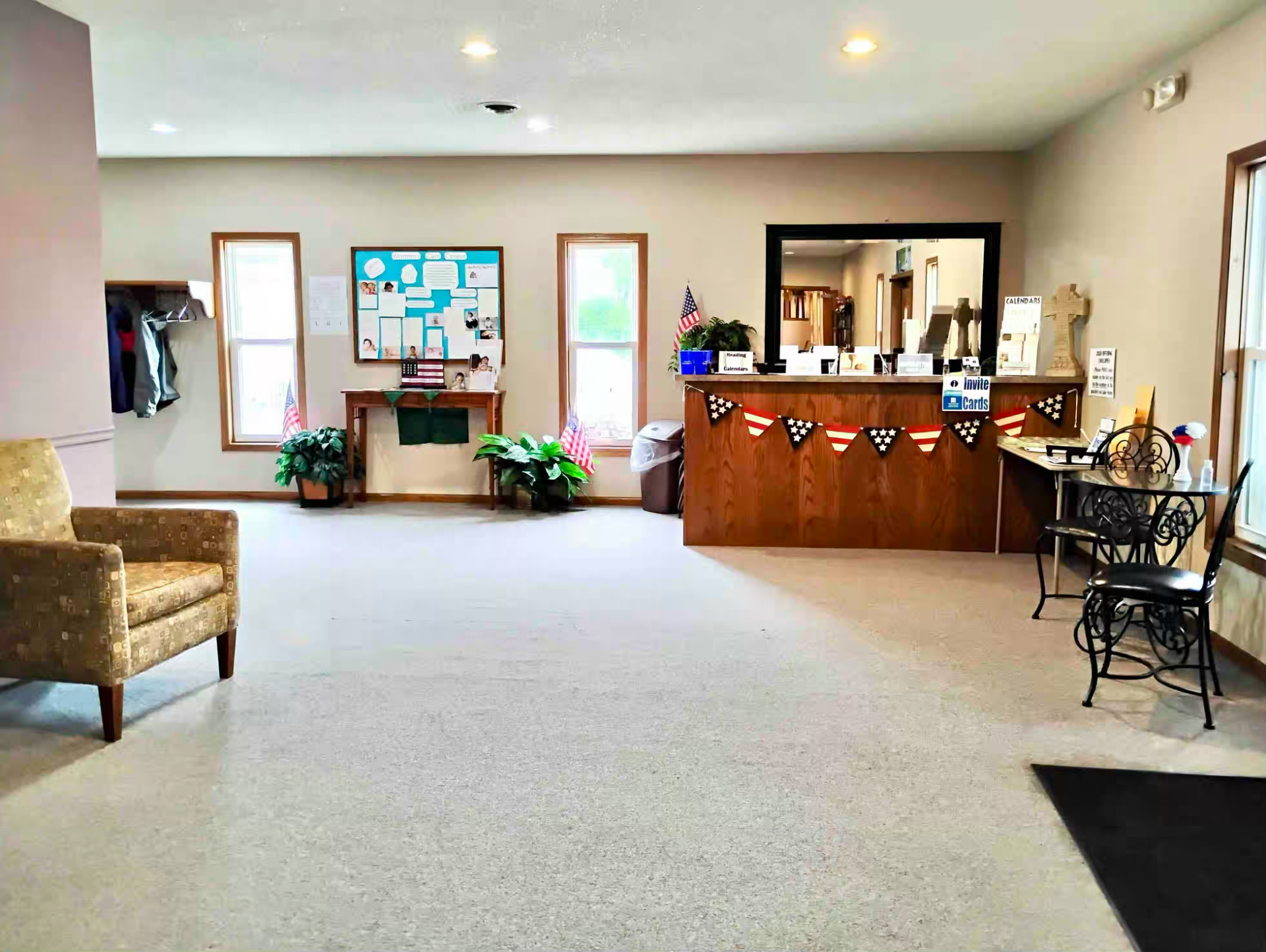 Reception area with decorated wooden desk, large mirror, bulletin board, and chairs.