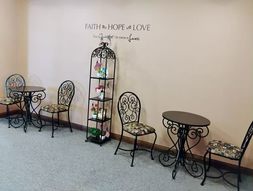 Decorative metal display stand with small floral arrangements, surrounded by bistro tables and chairs in a wide hallway.