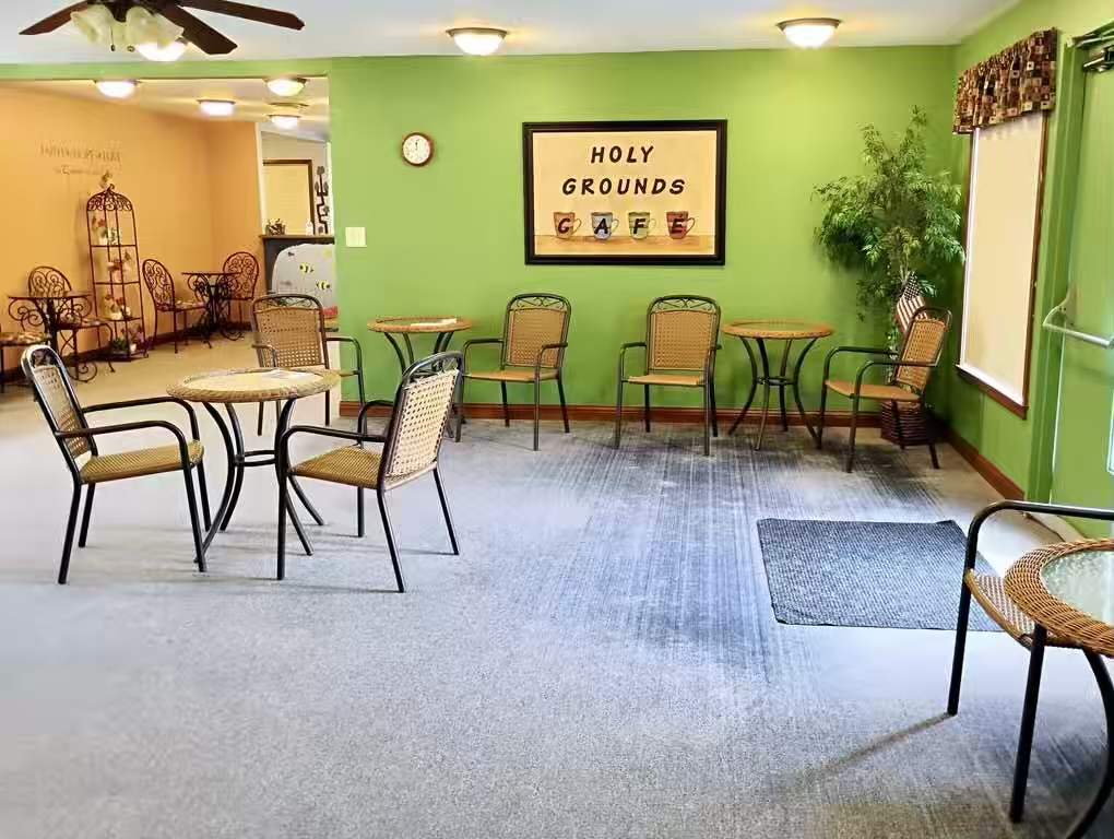 Bright green café seating area with bistro tables and chairs and “Holy Grounds Cafe” sign.