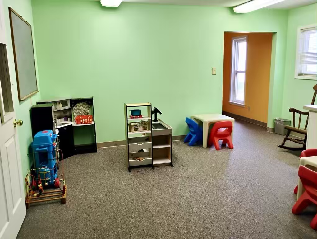 Bright green children’s playroom with toy kitchen set, small table and chairs, and wooden rocking chair.