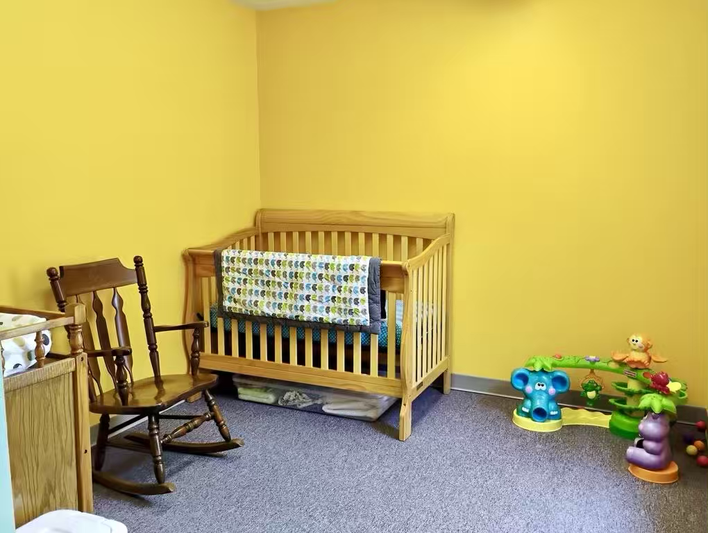 Bright yellow playroom with wooden baby crib, rocking chair, and colorful toys.