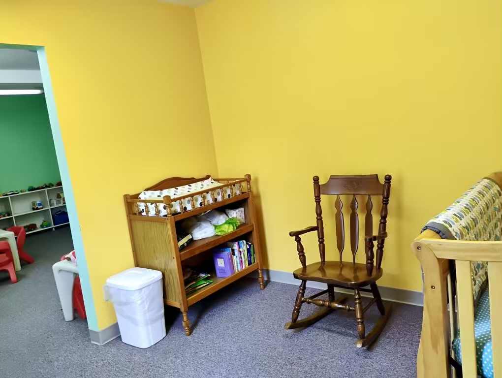 Bright yellow playroom with wooden rocking chair, changing table, and crib.