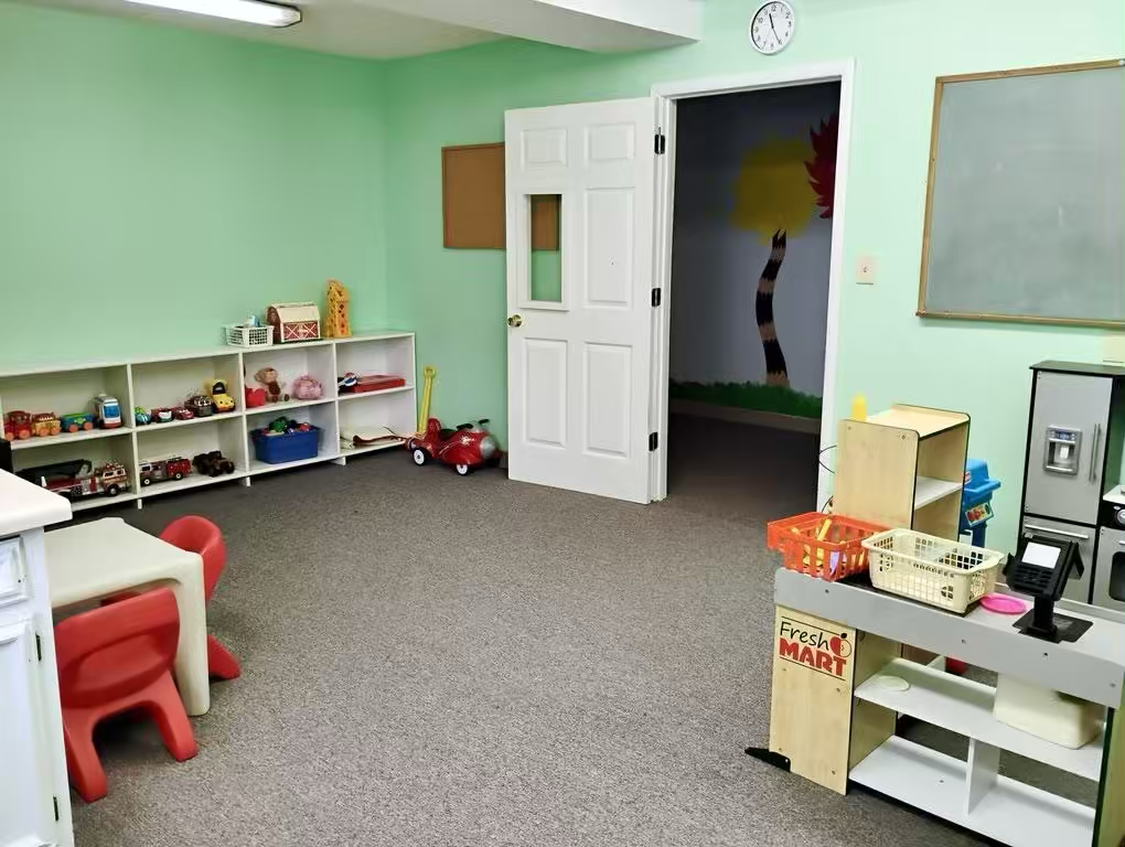Bright green children’s playroom with toys on storage shelves, toy kitchen set, and small table and chairs.
